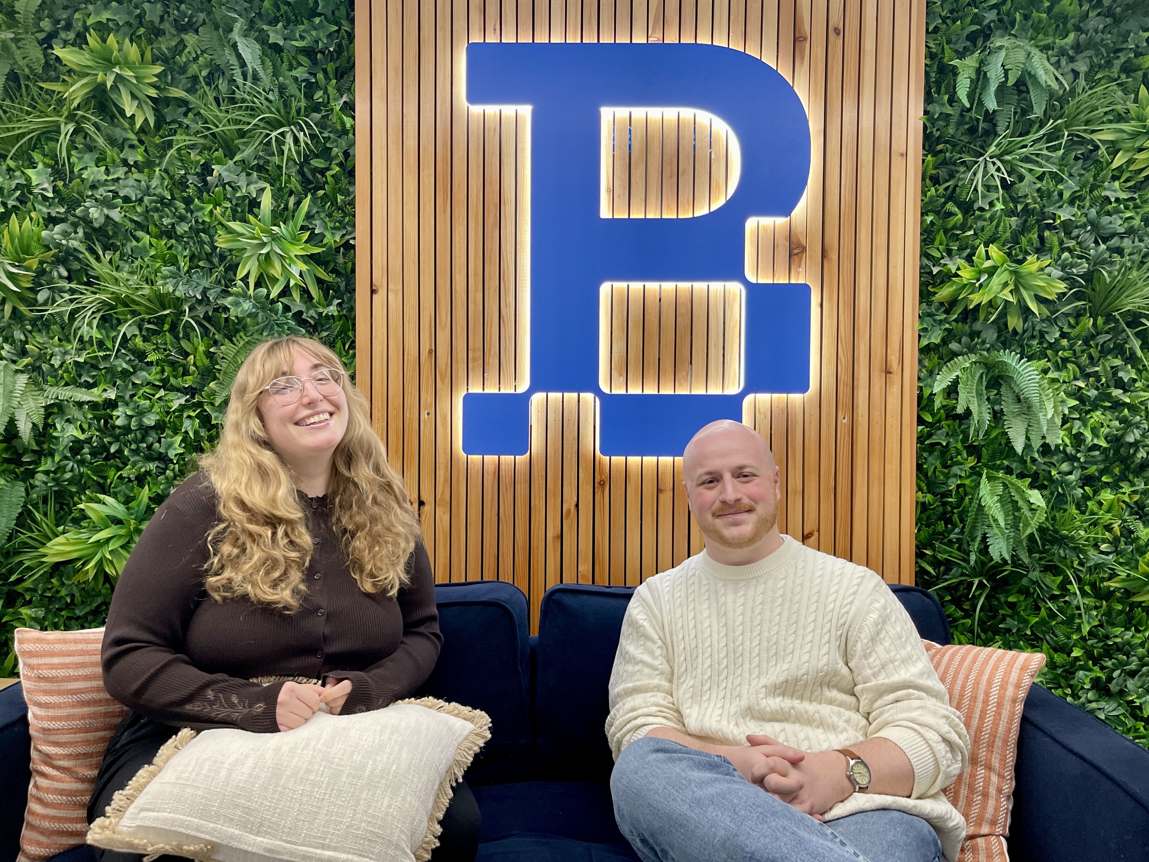 A woman and a man sat on a couch in an office setting.